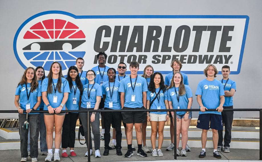 Group in blue Student TRACK t-shirts in front of Charlotte motor Speedway Sign